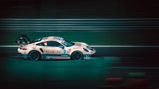 A sleek race car, adorned with various sponsor logos, speeds along a track. The motion blur effect across the image accentuates its high velocity. The scene is set against a backdrop of blurred horizontal lines typical of racing circuits.