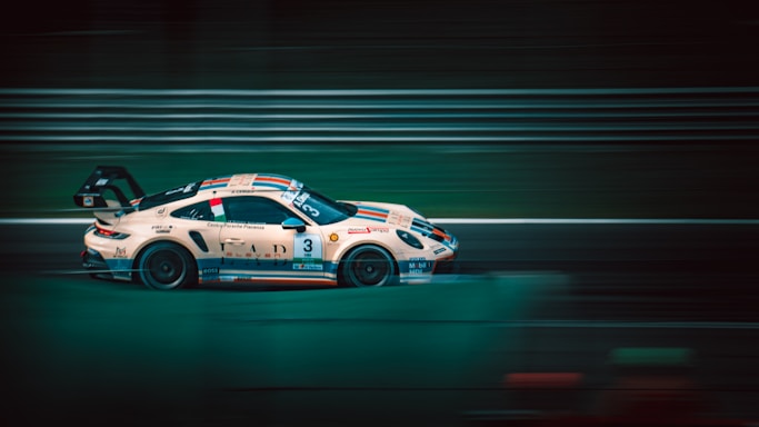 A sleek race car, adorned with various sponsor logos, speeds along a track. The motion blur effect across the image accentuates its high velocity. The scene is set against a backdrop of blurred horizontal lines typical of racing circuits.