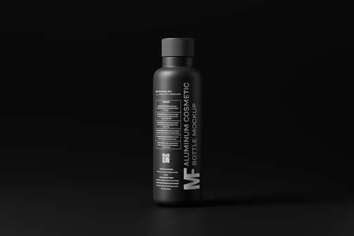 A sleek, matte black aluminum bottle stands against a dark background. The label features modern, minimalist typography in white, detailing the product as a cosmetic bottle mockup. The overall design conveys a luxurious and contemporary feel.