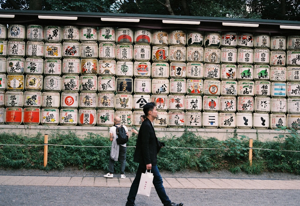 a man walking down a street past a wall covered in asian writing