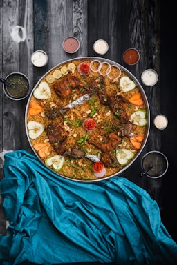 A vibrant platter showcasing assorted Afghan dishes including kebabs, pilaf, mantu dumplings, naan bread, and a bowl of sheer yakh dessert.