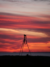 Tripod set up on rocky terrain with a sunset backdrop.