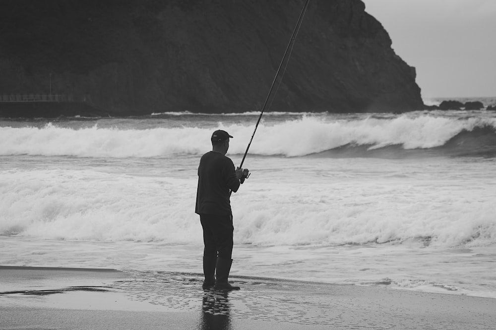 a man standing on top of a beach holding a fishing pole
