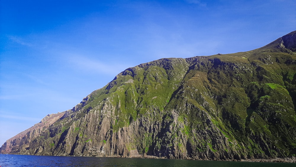 a large green mountain sitting next to a body of water
