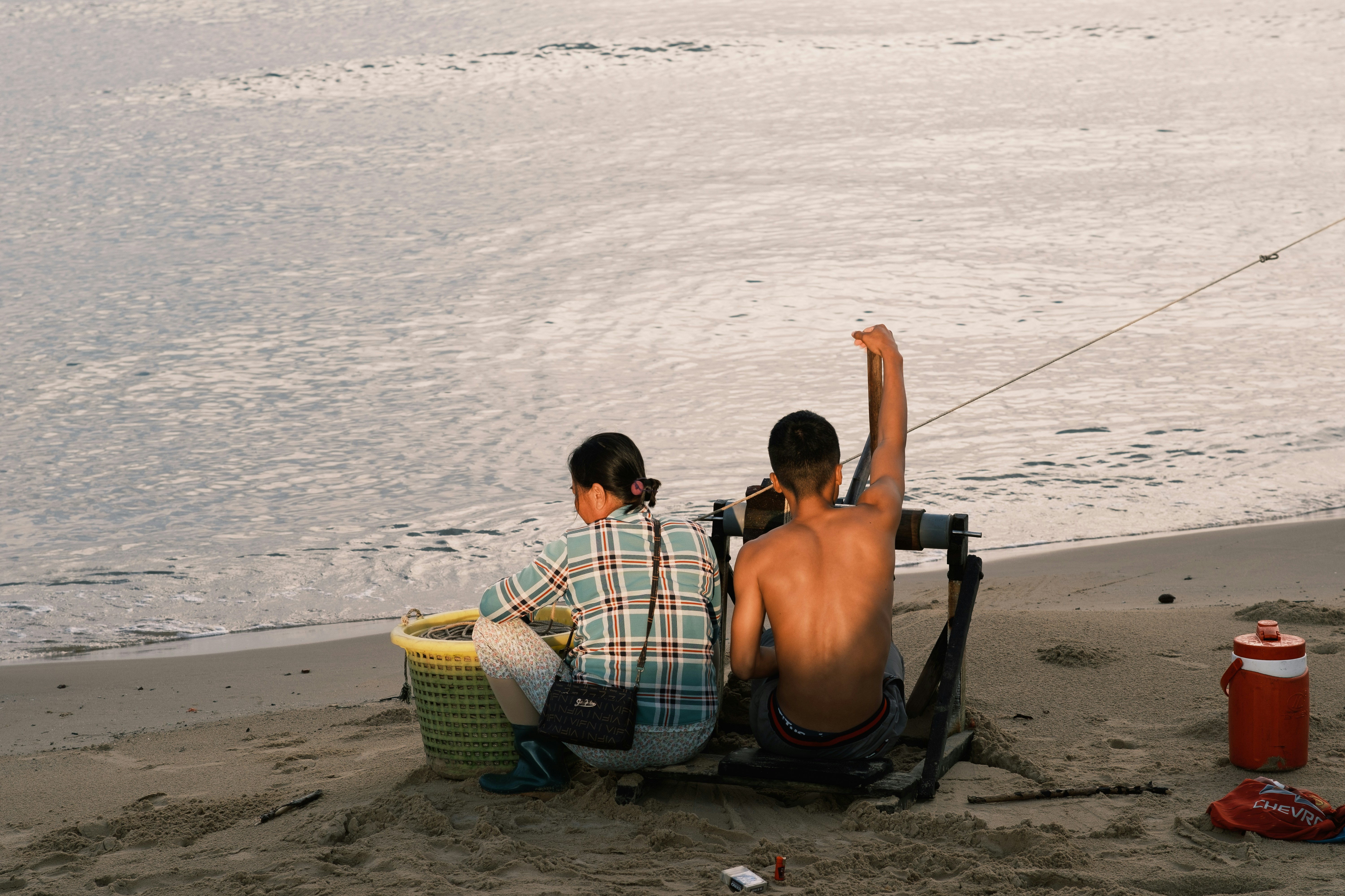 a couple of men sitting on top of a beach next to a body of water