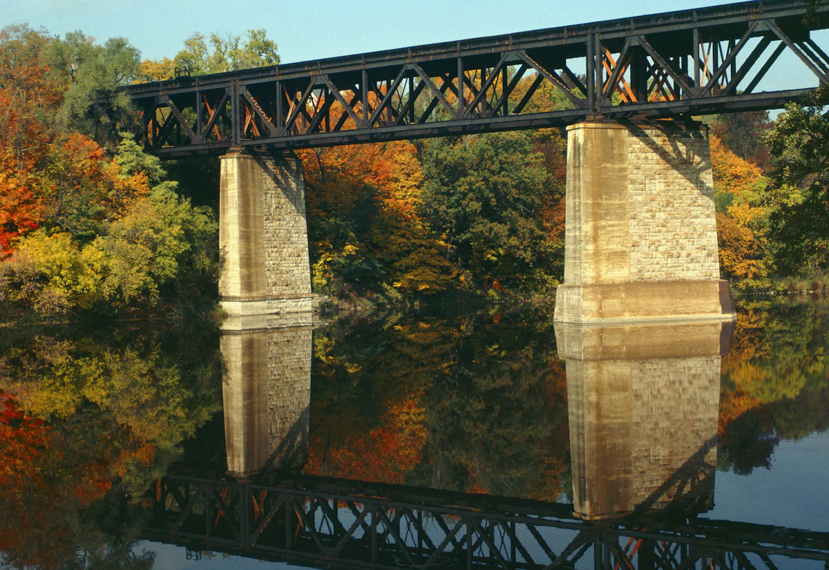 A steel railway bridge on stone piers over the Grand River at Paris, with autumn trees reflected