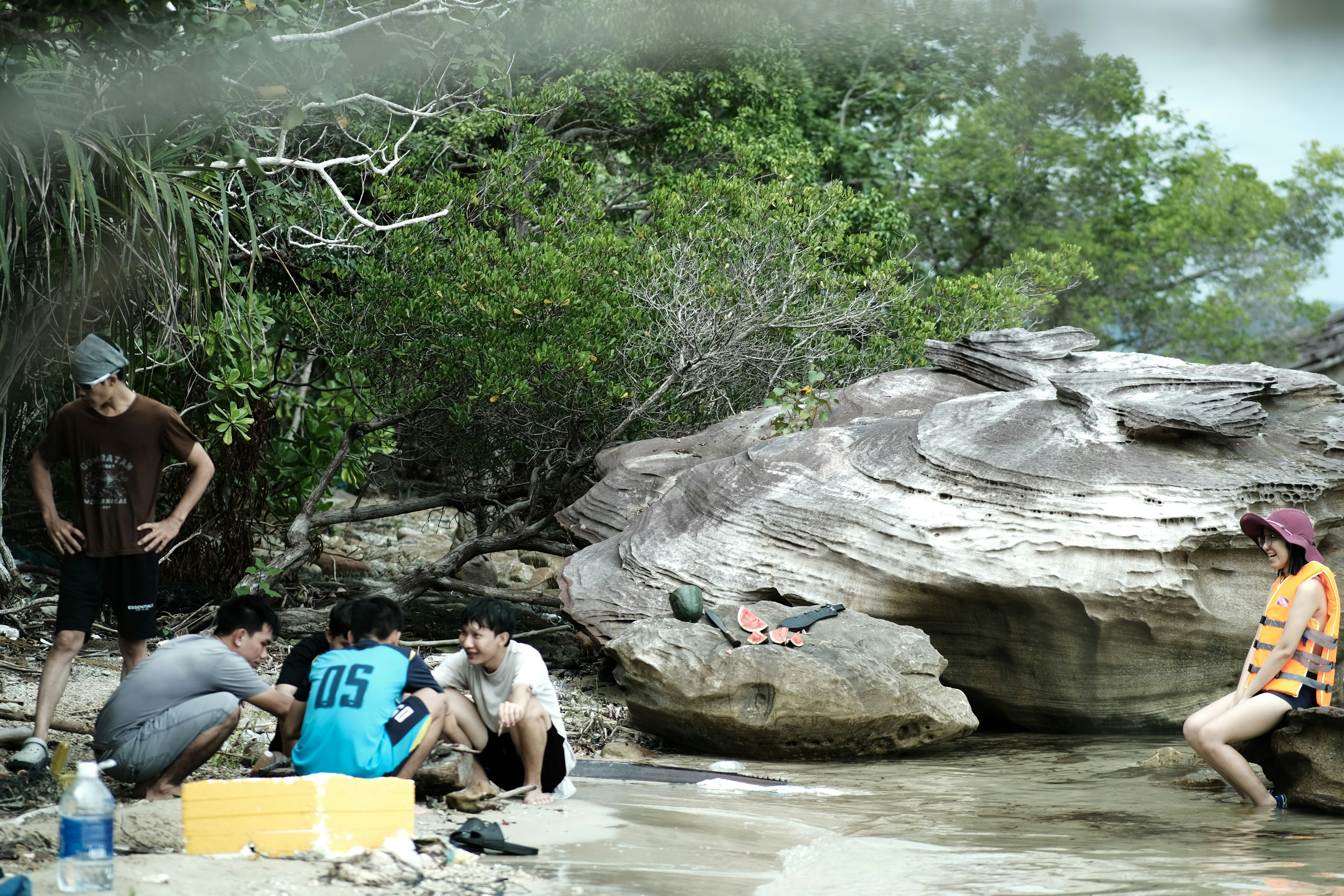 A group of people sitting on a beach next to a body of water photo ...