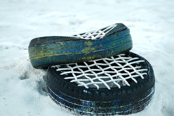 Two old tires are placed on a sandy surface, with their inner sections filled with a woven white rope netting. The tires appear weathered, showing paint chipping in colors of blue and green.
