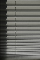 Horizontal window blinds casting layered shadows with alternating light and dark sections, forming a pattern on the surface.