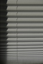 Horizontal window blinds casting layered shadows with alternating light and dark sections, forming a pattern on the surface.