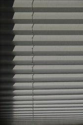 Horizontal window blinds casting layered shadows with alternating light and dark sections, forming a pattern on the surface.
