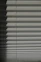 Horizontal window blinds casting layered shadows with alternating light and dark sections, forming a pattern on the surface.