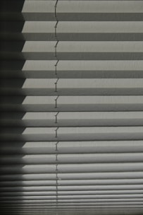 Horizontal window blinds casting layered shadows with alternating light and dark sections, forming a pattern on the surface.