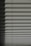 Horizontal window blinds casting layered shadows with alternating light and dark sections, forming a pattern on the surface.