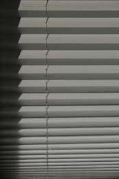Horizontal window blinds casting layered shadows with alternating light and dark sections, forming a pattern on the surface.