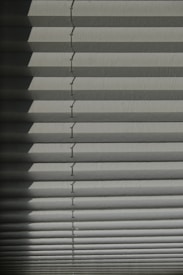 Horizontal window blinds casting layered shadows with alternating light and dark sections, forming a pattern on the surface.