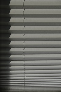 Horizontal window blinds casting layered shadows with alternating light and dark sections, forming a pattern on the surface.