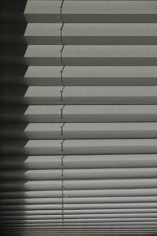 Horizontal window blinds casting layered shadows with alternating light and dark sections, forming a pattern on the surface.
