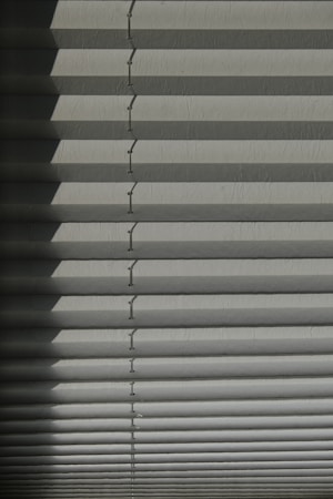 Horizontal window blinds casting layered shadows with alternating light and dark sections, forming a pattern on the surface.