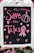 A blackboard with pink chalk writing features the phrase 'Save the Tatas' accompanied by decorative elements like hearts and a ribbon symbol often associated with breast cancer awareness. The board is framed in white and surrounded by a few blurred flowers at the bottom.