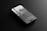 A sleek smartphone lying flat on a dark, reflective surface. The screen displays text and a grayscale image of a tower or building against a cloudy sky. The design of the phone appears modern with a thin profile and a visible front camera cutout.