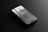 A sleek smartphone lying flat on a dark, reflective surface. The screen displays text and a grayscale image of a tower or building against a cloudy sky. The design of the phone appears modern with a thin profile and a visible front camera cutout.