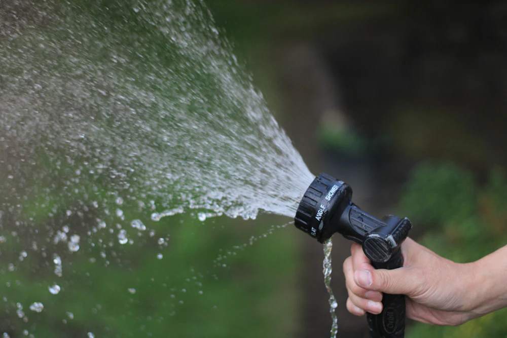 A hand spraying a strong stream of water from a garden hose