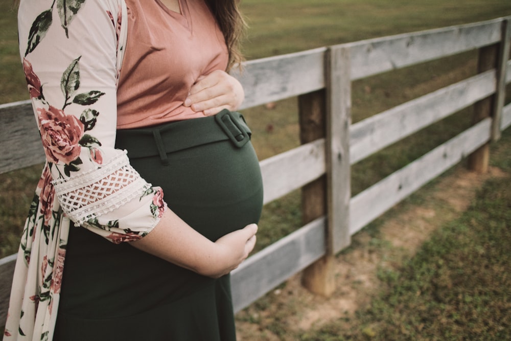 a pregnant woman standing in front of a fence