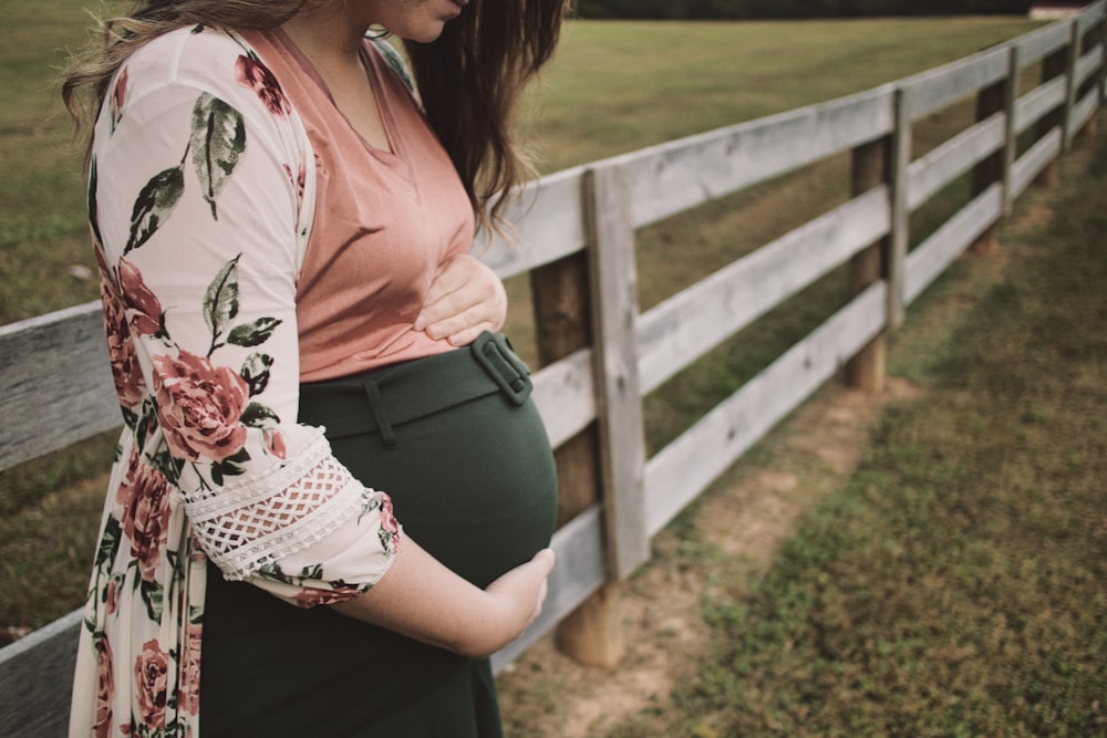 a pregnant woman leaning against a fence