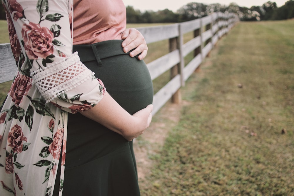 a pregnant woman standing next to a wooden fence