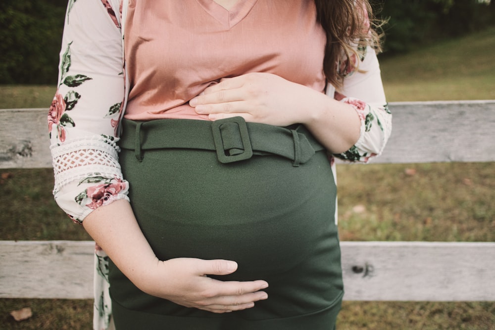 a pregnant woman standing in front of a fence