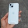 A hand is holding a white smartphone with dual cameras and an Apple logo on the back.
