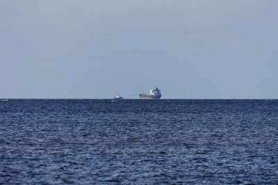 A stylized vector illustration of a cargo ship sailing across the ocean under a clear sky.