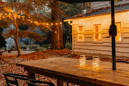 A wooden table set outdoors with mason jar centerpieces filled with wildflowers and twinkling fairy lights overhead.