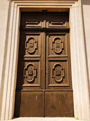A grand pivot door made of cocobolo wood and black forged steel set against a modern villa facade.