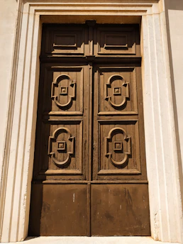 A grand pivot door made of cocobolo wood and black forged steel set against a modern villa facade.