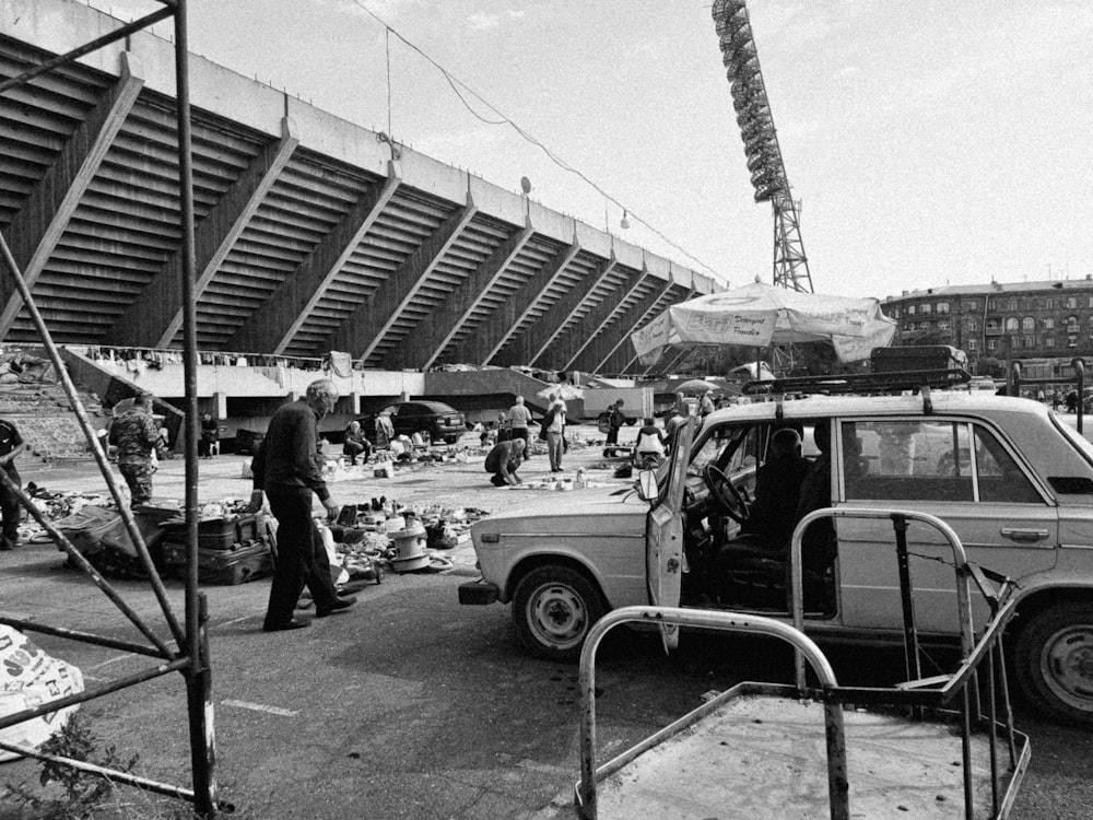 a black and white photo of a car parked in front of a stadium