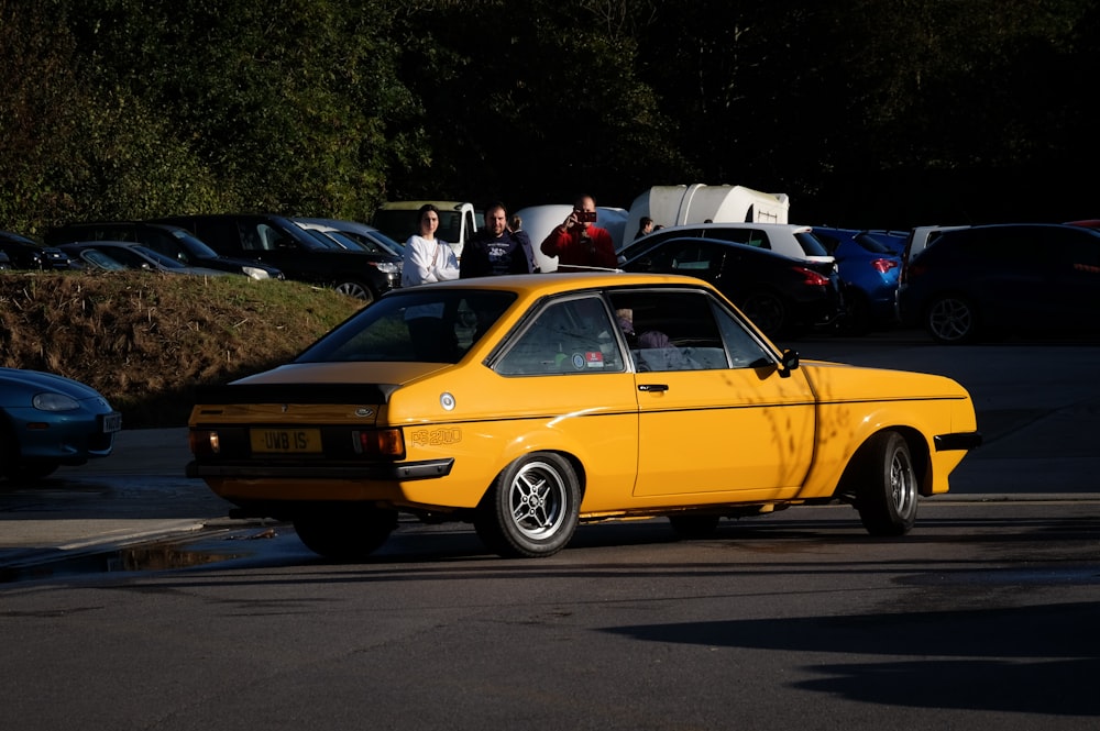 a yellow car driving down a street next to parked cars