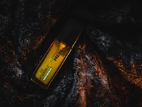 A bottle of Garnier Men Vitamin C+ serum gel lies atop a textured, dark, and fur-like fabric. The label on the bottle is highlighted in contrasting light, making the green and white text stand out against the yellow bottle.