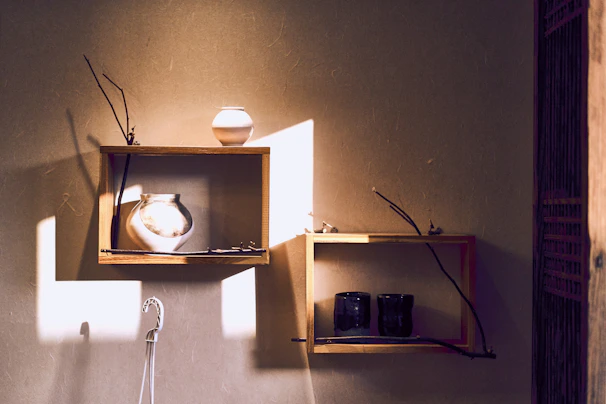 Sunlight filtering through a window onto a shelf displaying sky blue and terracotta vases with organic shapes.