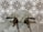 Antique bronze taps mounted on a marble wall with intricate patterned tiles in the background. The design of the tiles is ornate, featuring symmetrical floral motifs in dark brown and white.