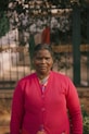 a woman in a pink cardigan standing in front of a fence