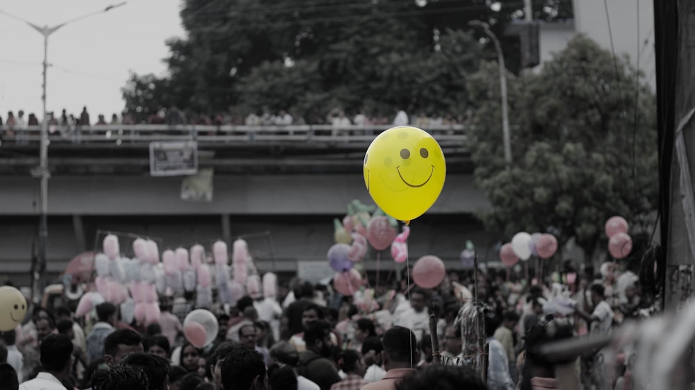 a smiley face balloon floating in the air above a crowd of people