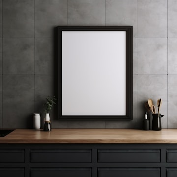 A minimalistic kitchen setting with a wooden countertop. A blank white framed board is hung on a gray tiled wall. On the counter, various kitchen items like vases and cooking utensils are neatly arranged.