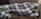 A couch is covered by a large, soft blanket with a checkered pattern in shades of gray and white. There is a decorative pillow with a circular design next to it.