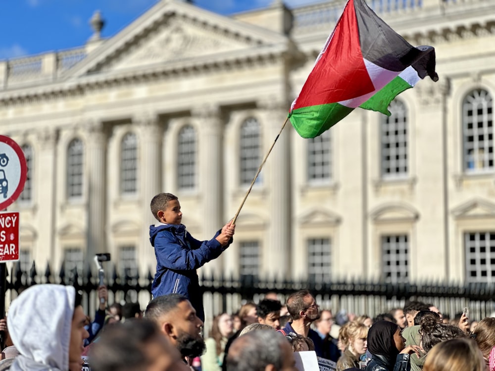 a young boy holding a flag in front of a crowd of people