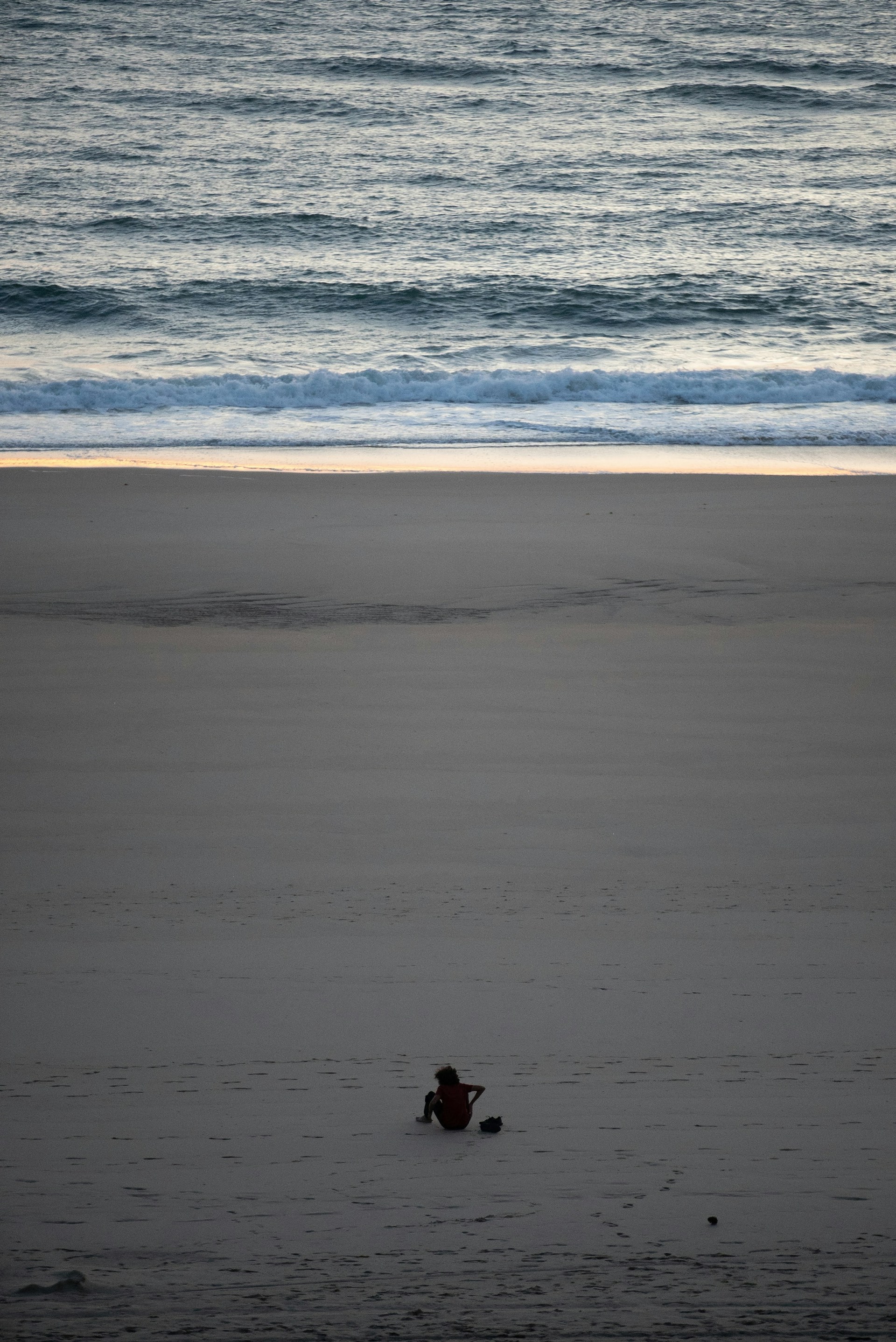 A peaceful beach scene with a lone traveler sitting on the sand, gazing out at the endless ocean horizon.
