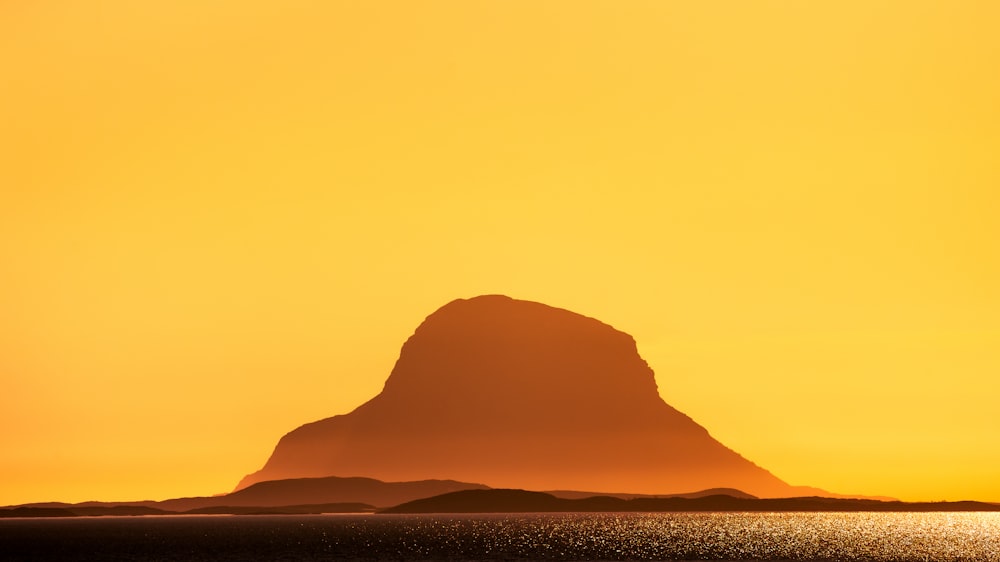a large mountain in the distance with a yellow sky