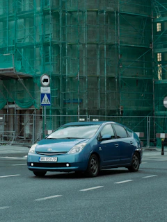 a blue car driving down a street next to a tall building