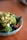 A bowl filled with a variety of fresh, healthy ingredients including chopped avocado, broccoli, blueberries, and what appears to be kale. The dish is garnished with red pepper flakes and sits on a wooden surface.